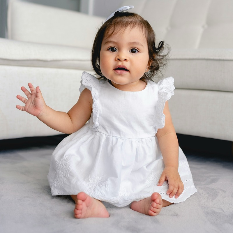 Baby girl in a white eyelet dress sitting on a soft rug | Bundled add-on formal wear, gently-loved baby dresses and special occasion outfits in Canada