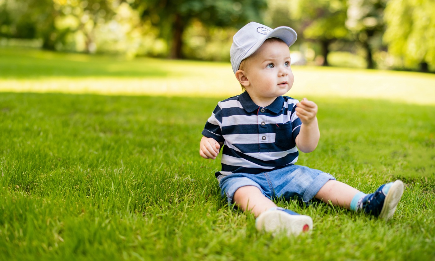 Baby boy in a striped polo and ball cap sitting in green grass on a sunny day | Bundled sustainable childrenswear Canada, eco-friendly gently-loved baby clothes
