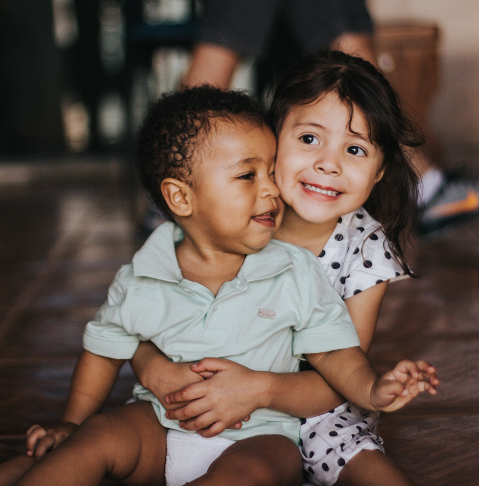 Siblings hugging on the kitchen floor in comfy play clothes | Bundled eco-friendly kids clothing, reducing textile waste with gently-loved baby bundles